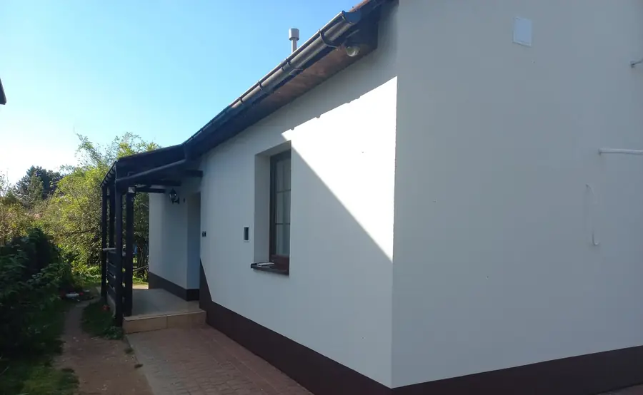 Narożnik domu z ciemną rynną i rurą spustową na jasnej elewacji